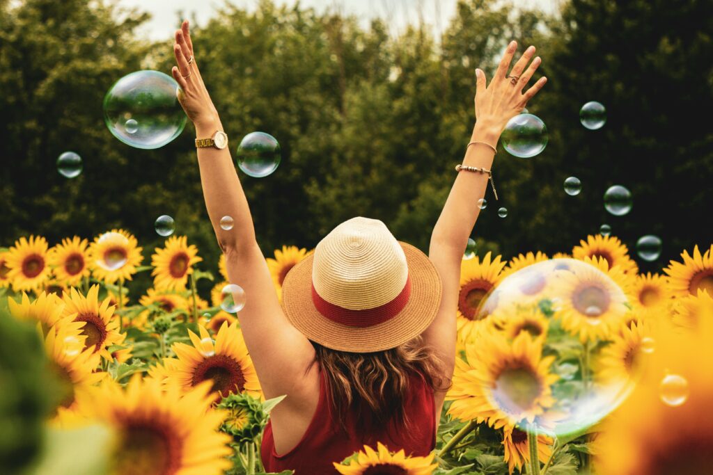 A woman with her arms raised standing amidst soap bubbles in a field of sunflowers